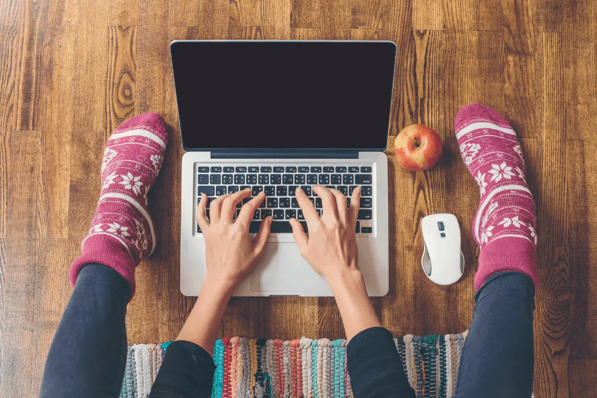 a woman typing on a laptop on the floor with pink socks on