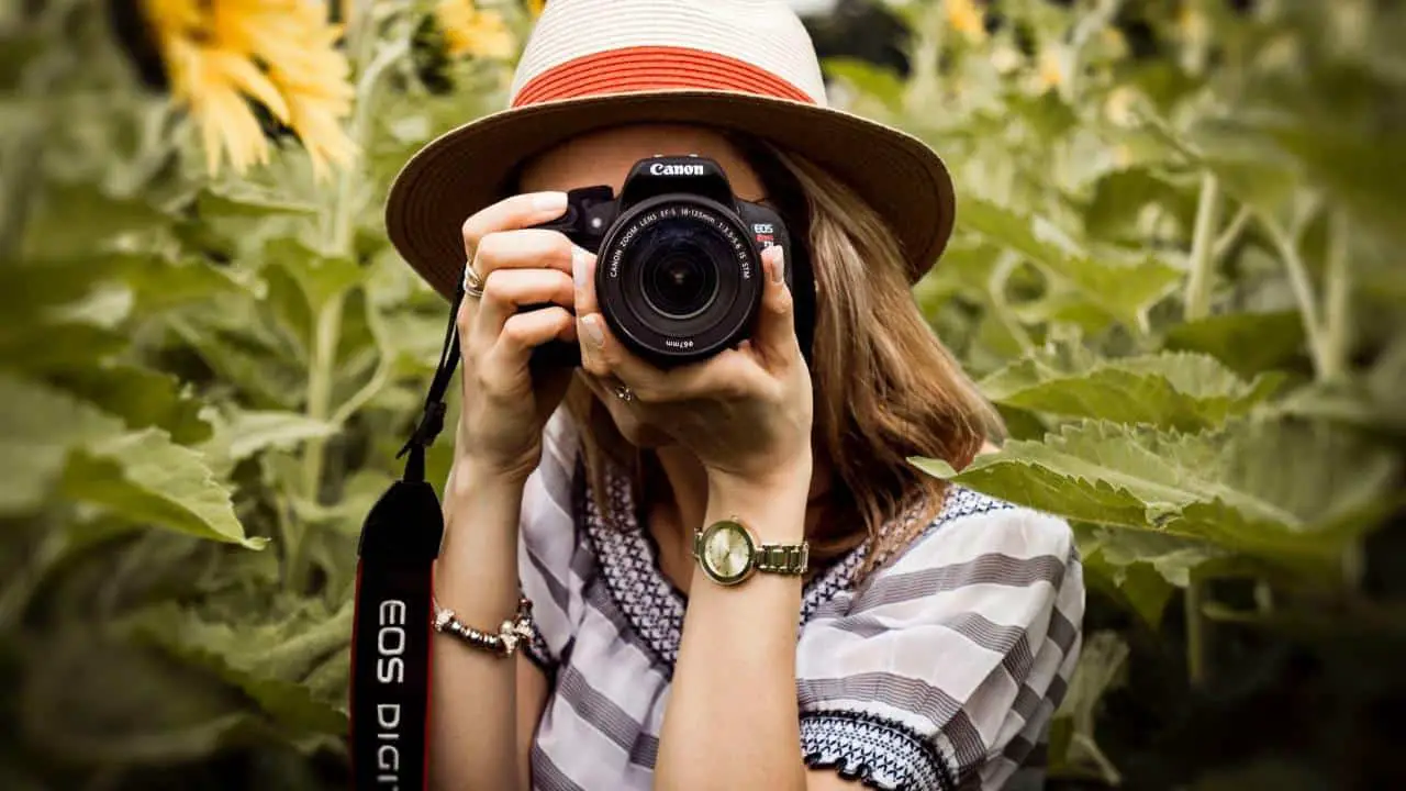 a photo of a woman pointing a camera at the camera with green trees behind