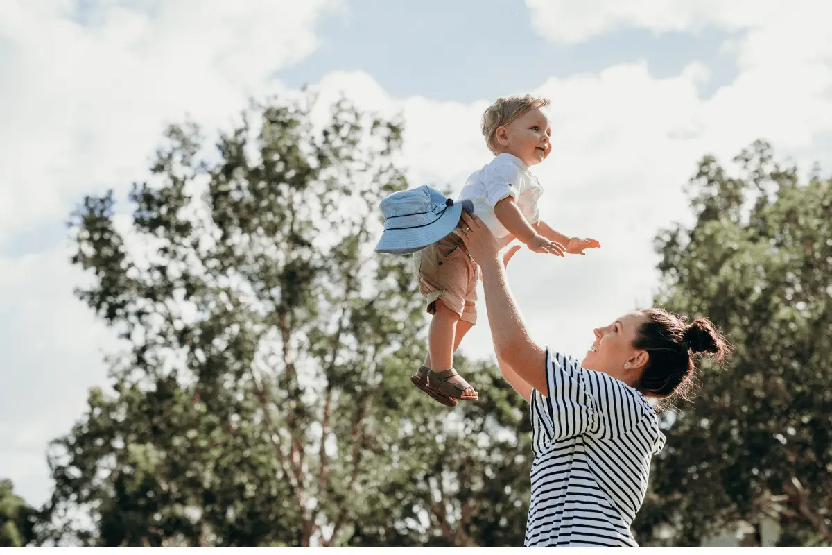 a woman holding a child up in the air with trees in the background