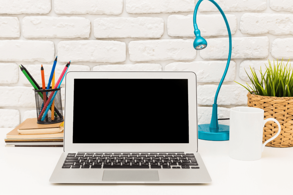 Macbook pro青いランプ、白いコーヒーマグ、植物とその隣に色鉛筆の容器と白い机の上に。