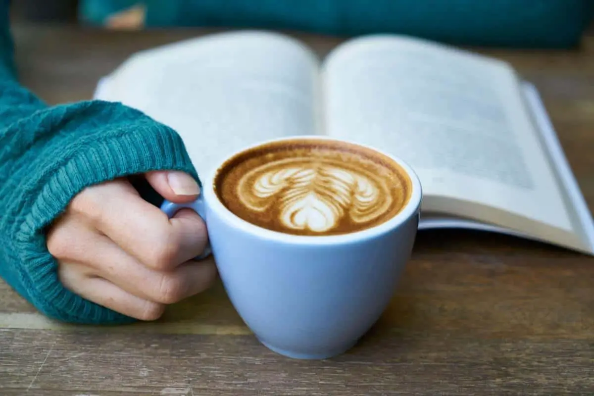 hand holding book and a cup of coffee