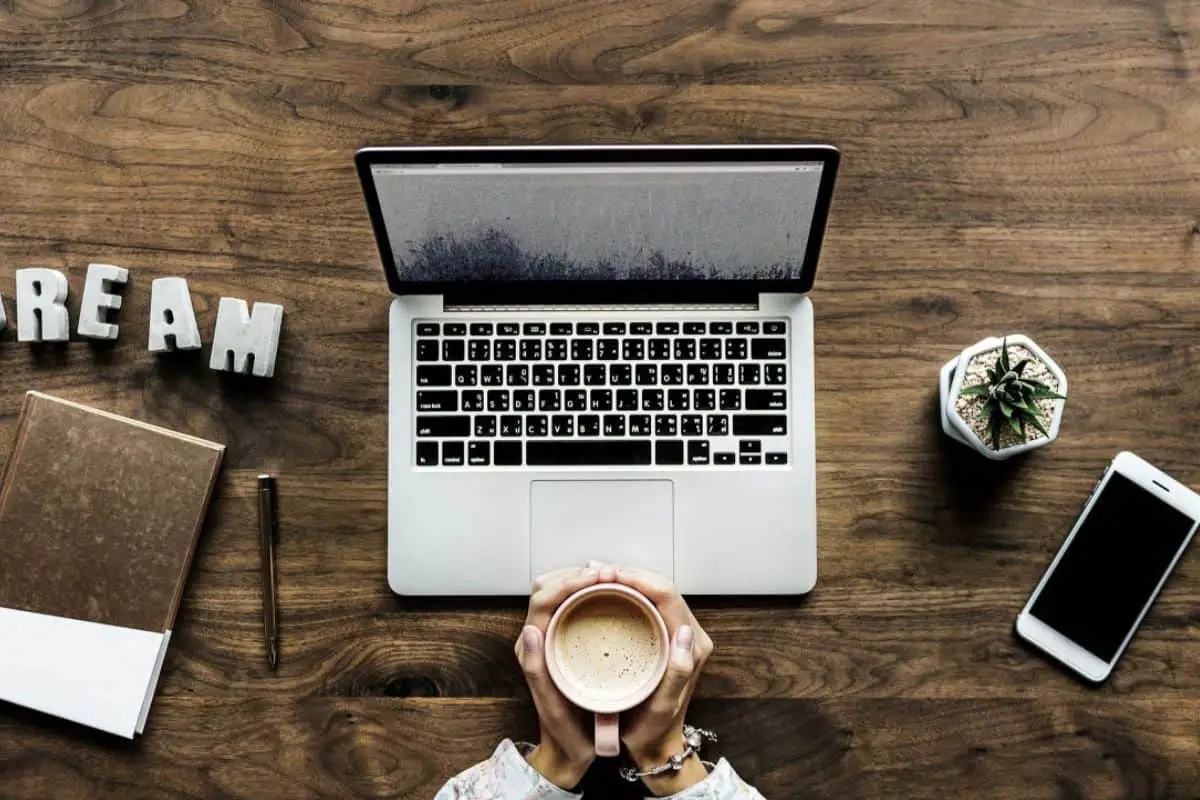 hands holding a cup of coffee in front of a laptop