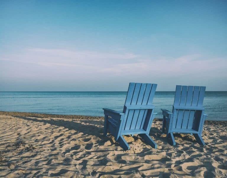 photo of a beach with two blue beach chairs on the sand