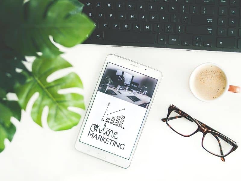 a smartphone sitting on a desk with a pair of glasses and a plant in the background