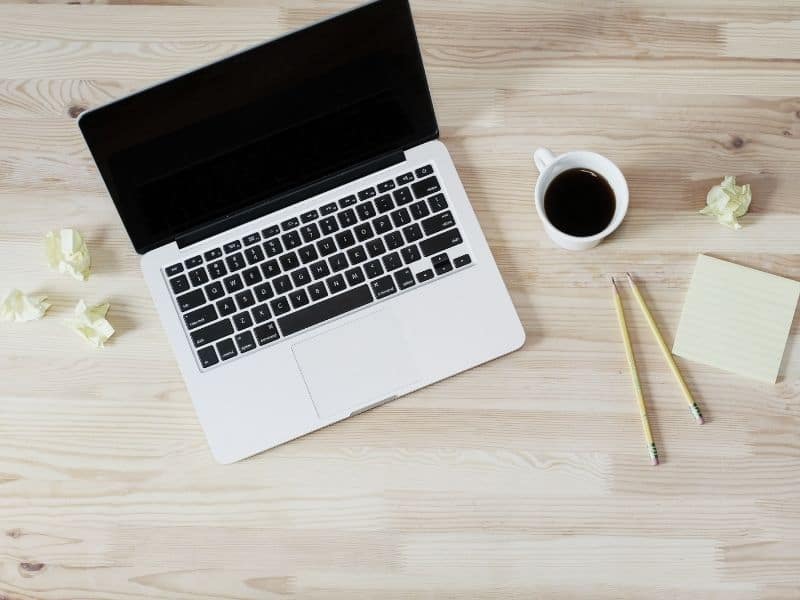 computer on a wood desk with a cup of coffee and 2 pencils