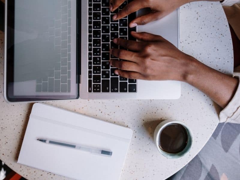 womans hands typing on laptop with a cup of coffee