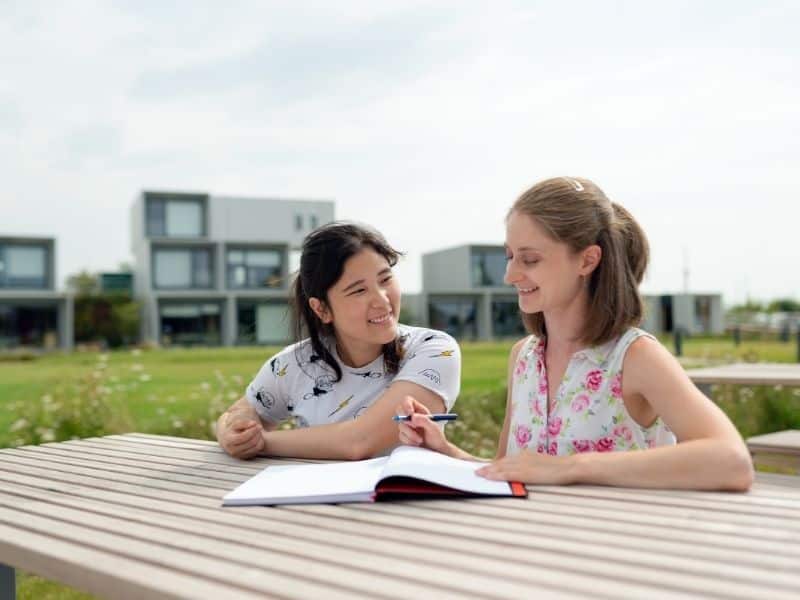 2 kids sitting at a table outside looking at a book