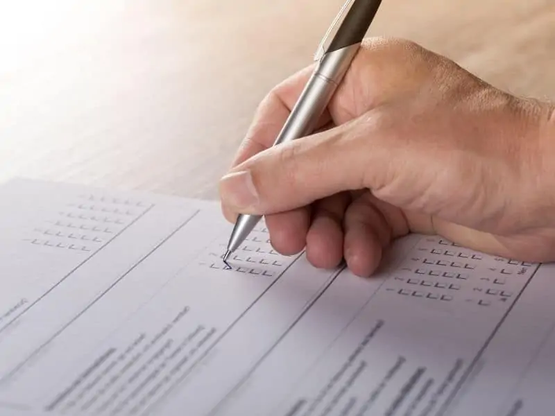 a human hand holding a pen filling out a paper survey