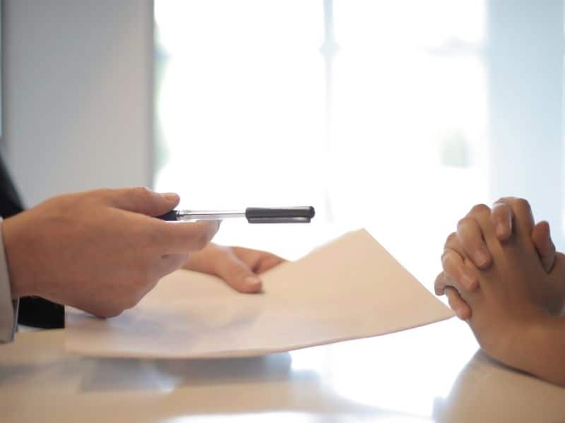 hans passing a piece of paper and pen over to another set of hands