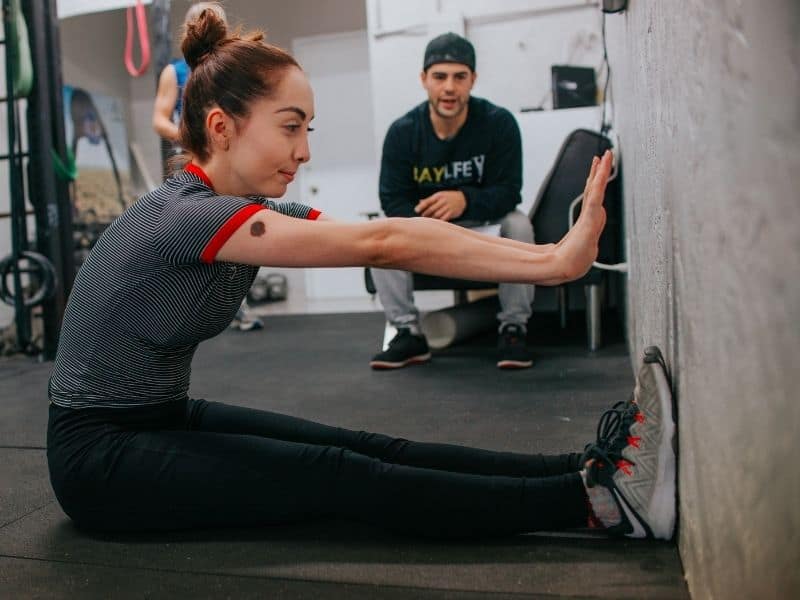 a woman in a gym sitting with her arms out towards a wall