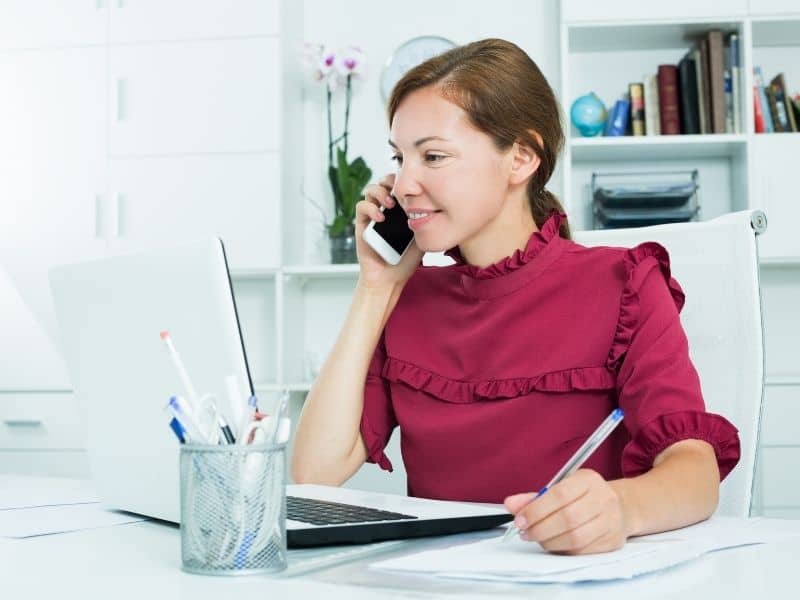 a woman on the phone sitting in front of a computer in a pink shirt