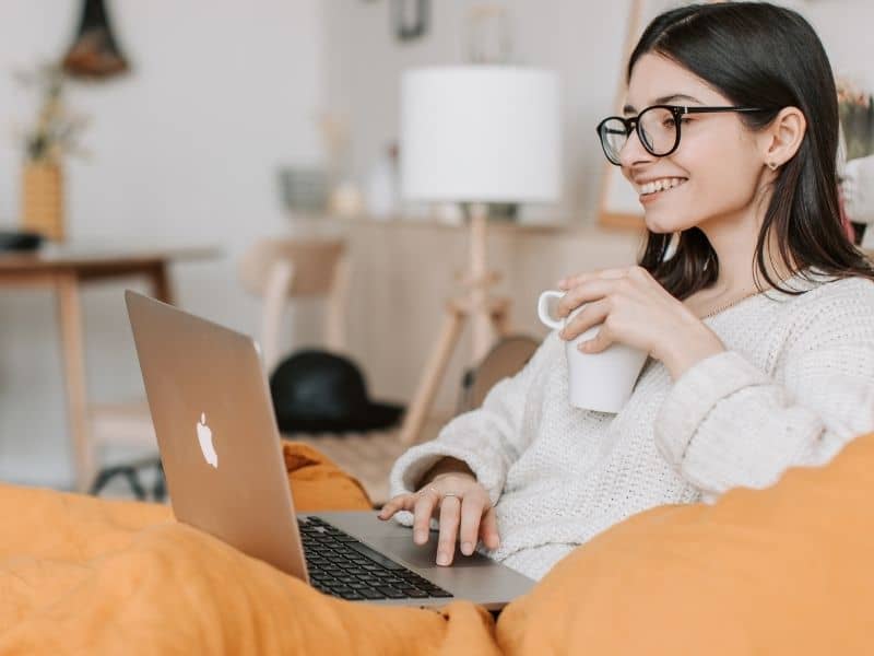 a woman holding a cup of coffee with a laptop in her lap working