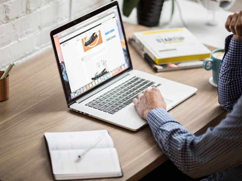 a laptop on a desk with a notebook and someone typing