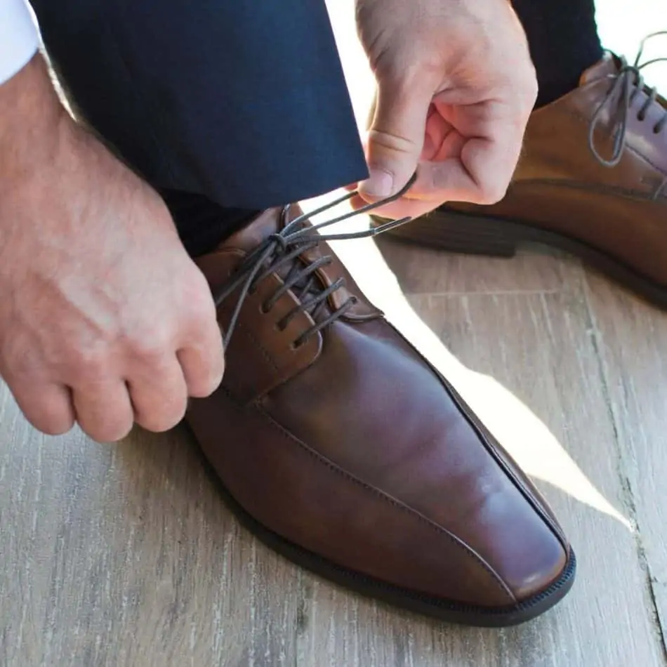 a man tying his brown dress shoe