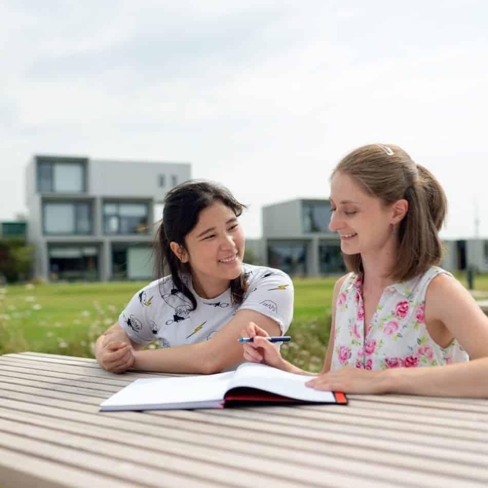 2 women sitting at a picnic tables with a book in front of them