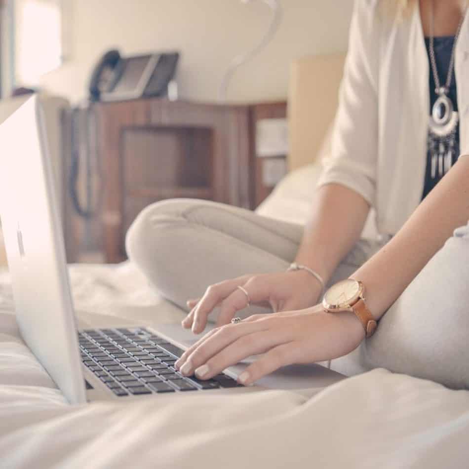 a woman sitting on a bed typing on a laptop