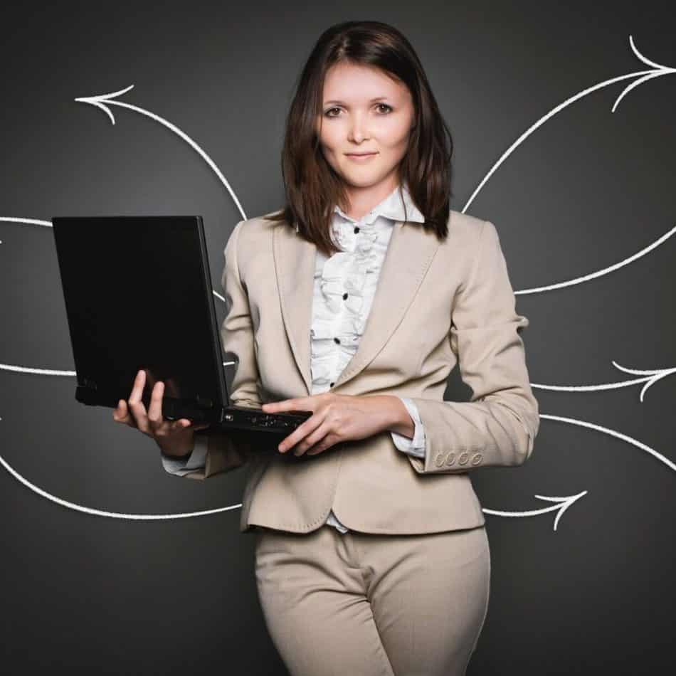 a woman in a tan suit holding a laptop looking at the camera