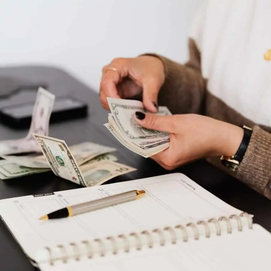 a woman counting money over a notebook on a desk
