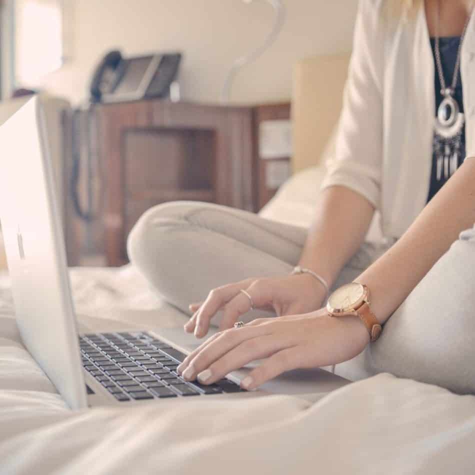 a woman sitting on a bed typing on a laptop