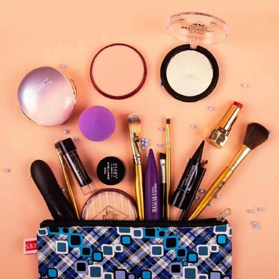 a makeup bag laying on a pink surface with makeup spilling out